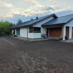 Piotr - Przygotowany teren pod trawnik przed nowoczesnym domem z garażem i motocyklem. Widoczne ślady opon na ziemi i narzędzia ogrodnicze. Etap prac ogrodniczych.