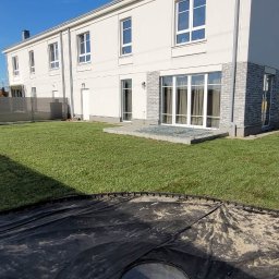 Piotr - Świeżo ułożony trawnik z rolki przed nowoczesnym domem. Widoczny fragment przygotowanego terenu pod dalsze prace, ogrodzenie w tle i błękitne niebo.