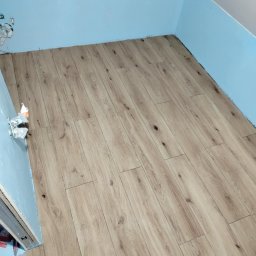 Usługi ogólno-budowlane - Ukończona podłoga z paneli drewnopodobnych w pokoju z niebieskimi ścianami. Widoczne niedokończone wykończenia przy ścianach i instalacji.