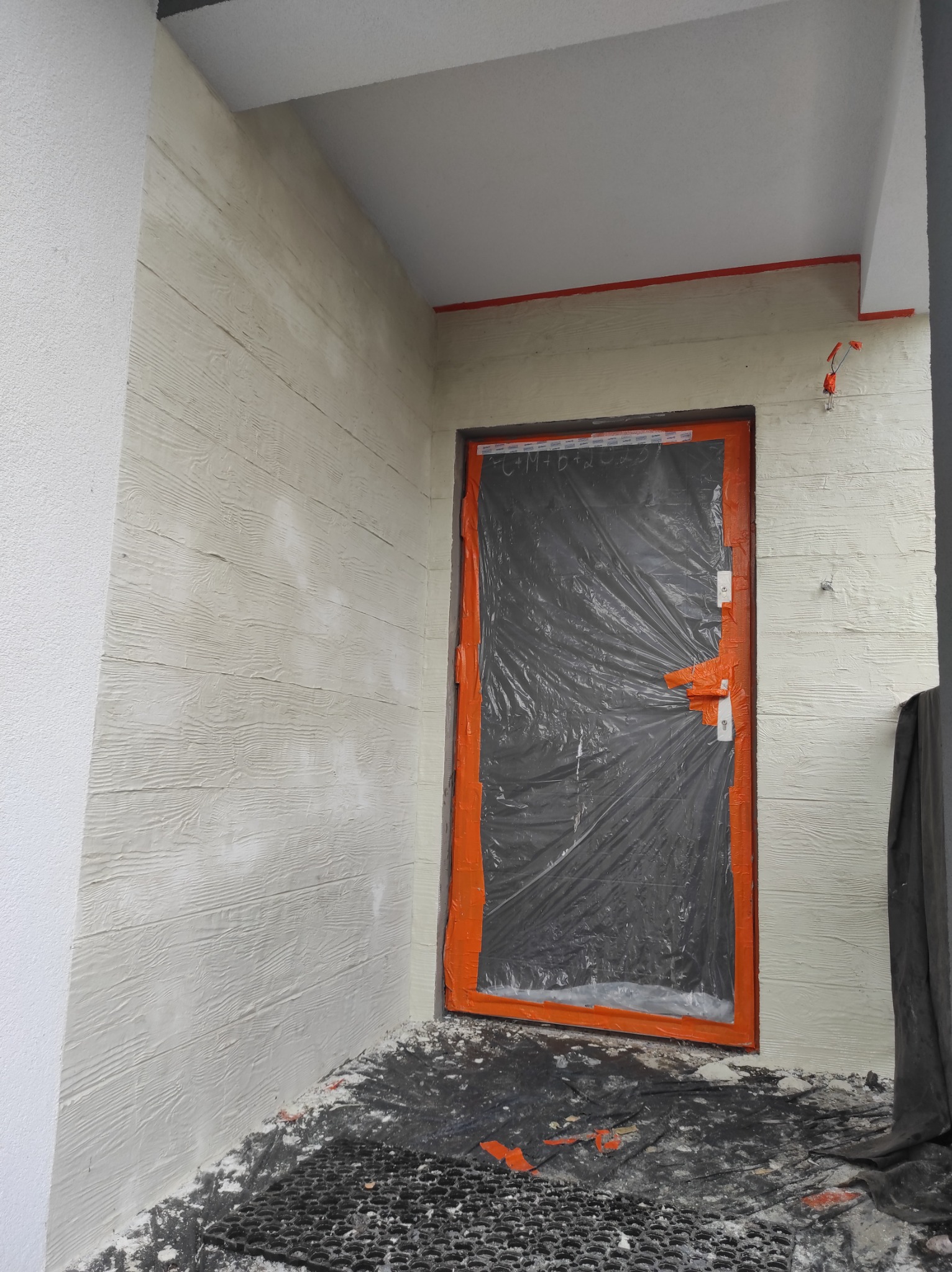 Elewacja z fakturą drewna, zabezpieczone okno folią malarską. Detal wykończenia ściany zewnętrznej z widoczną strukturą desek. Prace malarskie w toku.