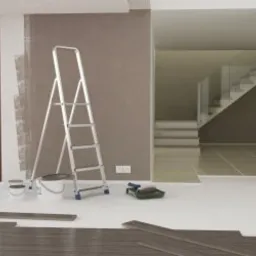 Wnętrze w trakcie remontu: drabina oparta o ścianę z częściowo pomalowaną powierzchnią, puszki z farbą, wałek malarski, panele podłogowe przygotowane do ułożenia, widok na schody w tle.