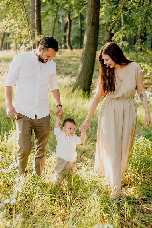 Rodzina spaceruje po lesie trzymając się za ręce, rodzice prowadzą małe dziecko, ciepłe, naturalne światło.
