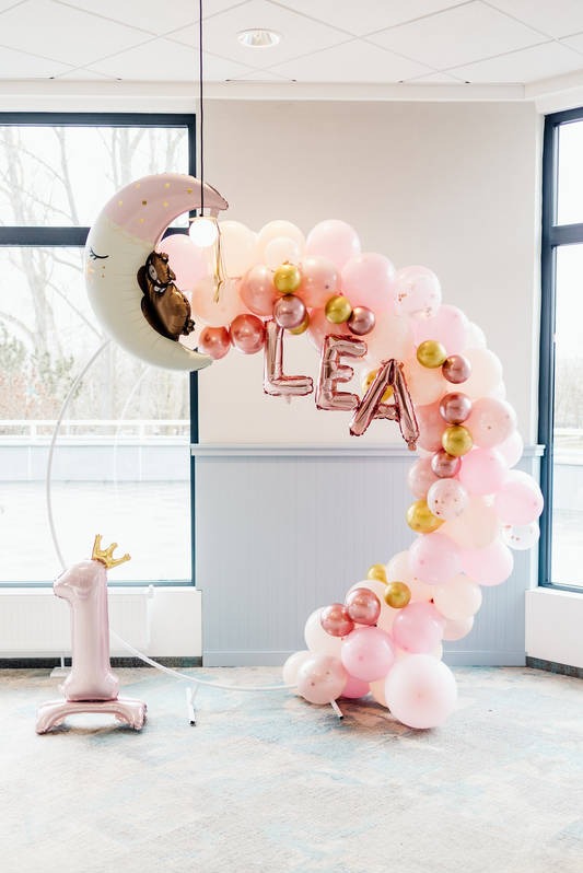 Dekoracja balonowa na pierwsze urodziny dziecka: łuk z różowych i złotych balonów, balon w kształcie księżyca z misiem i cyfra '1' z koroną.