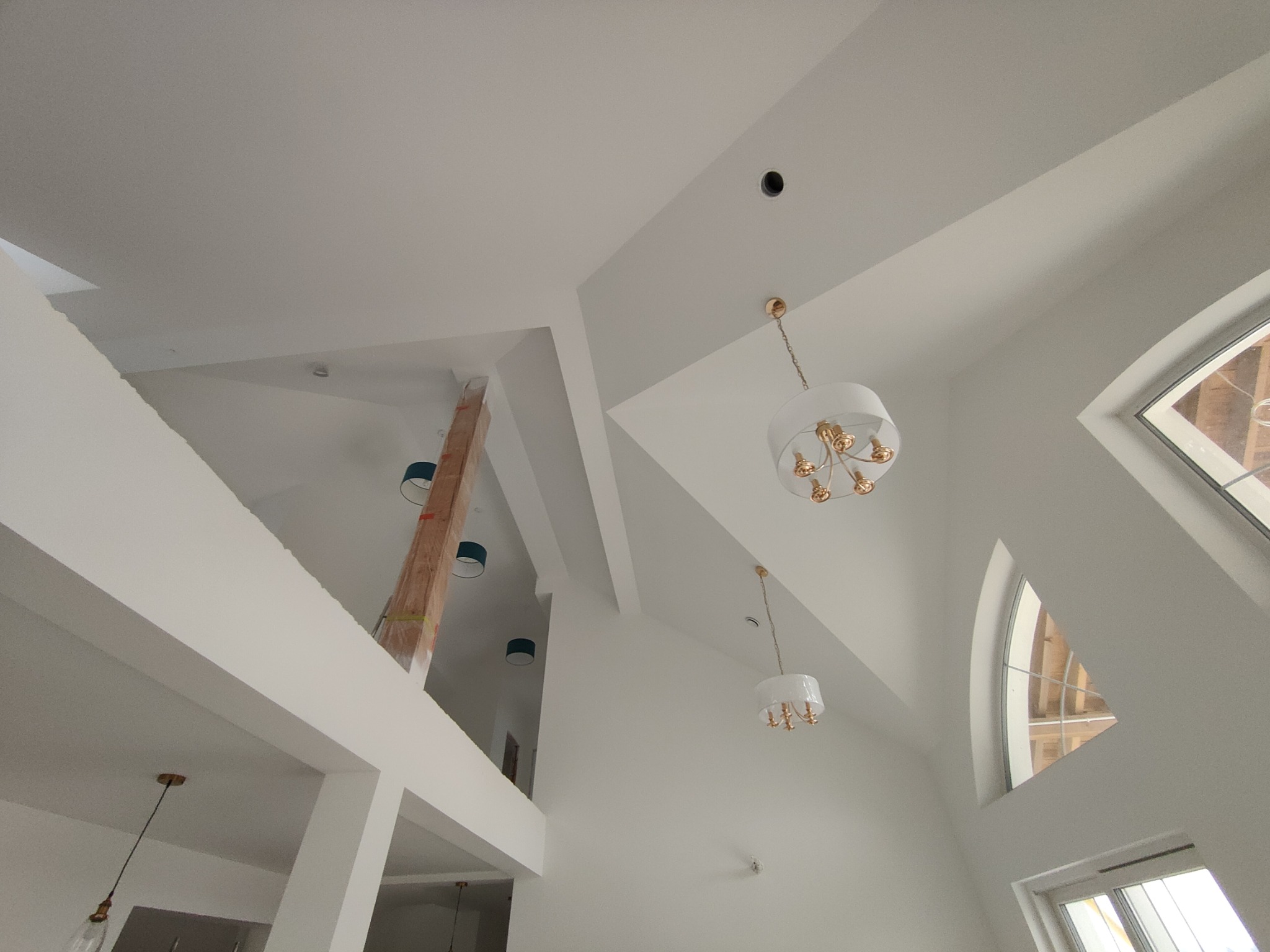 Wysoki salon z białymi ścianami i stropem, drewnianą kolumną w tle oraz nowoczesnymi lampami wiszącymi. Widok z dołu ukazuje geometrię pomieszczenia.