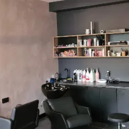 Wnętrze salonu fryzjerskiego z czarnymi meblami, umywalką, lustrem i żółtymi tulipanami w wazonie, widoczne półki z kosmetykami i akcesoriami.