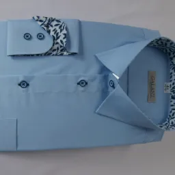 Jasnoniebieska, elegancko złożona koszula męska z długim rękawem, z mankietami i kołnierzykiem wykończonymi wzorem w ciemne liście na białym tle, widoczny rozmiar 44 na metce.