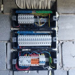 Rozdzielnia elektryczna z zabezpieczeniami przepięciowymi i wyłącznikami zamontowana na ścianie z bloczków betonowych w Żywcu, widoczne okablowanie i elementy mocujące.