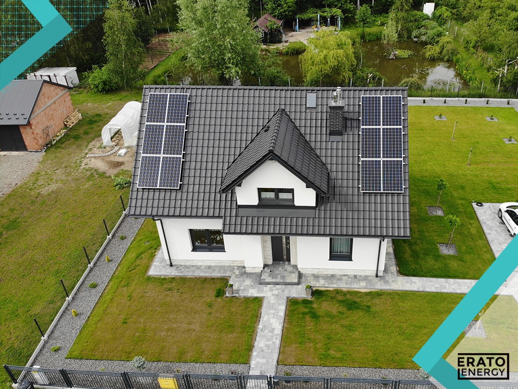 Widok z góry na dom jednorodzinny z panelami fotowoltaicznymi na dachu, w tle staw i zieleń, logo firmy Erato Energy w rogu.