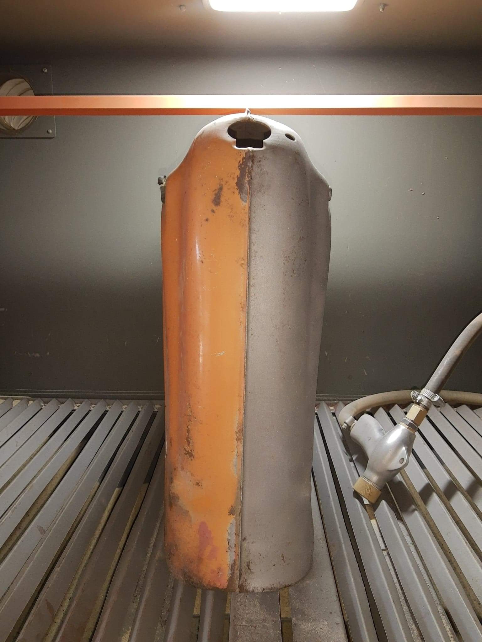 Metalowy zbiornik w połowie oczyszczony z rdzy i starej farby, widoczny pistolet do piaskowania, wnętrze kabiny z kratownicą.