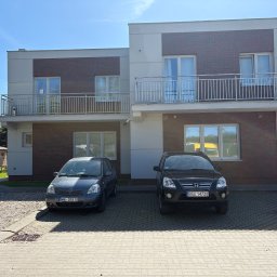 Mix-Bud - Dwupiętrowy budynek z ceglaną elewacją i balkonami, dwa samochody zaparkowane przed budynkiem na kostce brukowej, słoneczny dzień.