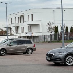 Mix-Bud - Nowoczesny, trzypiętrowy budynek z białymi elewacjami i regularnym układem okien, widziany z parkingu z dwoma samochodami w kadrze, przy pochmurnym niebie.