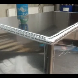 Szczegółowe zbliżenie na spawany narożnik metalowej konstrukcji, ukazujący precyzyjne spoiny w kształcie łezek, z widocznymi śladami obróbki i refleksami światła.