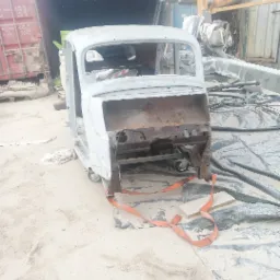 Karoseria samochodu po oczyszczeniu z rdzy, przygotowana do dalszej obróbki, widoczny transportowy pas zabezpieczający i fragment kontenera w tle.