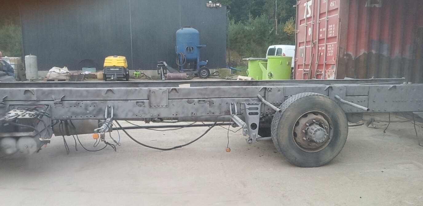 Rama pojazdu ciężarowego po obróbce, widoczna szara, matowa powierzchnia. W tle kontener, zbiorniki i maszyny.