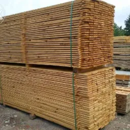 Stosy świeżo przetartego drewna ułożone na paletach, zabezpieczone zieloną taśmą, widoczne ślady po cięciu.