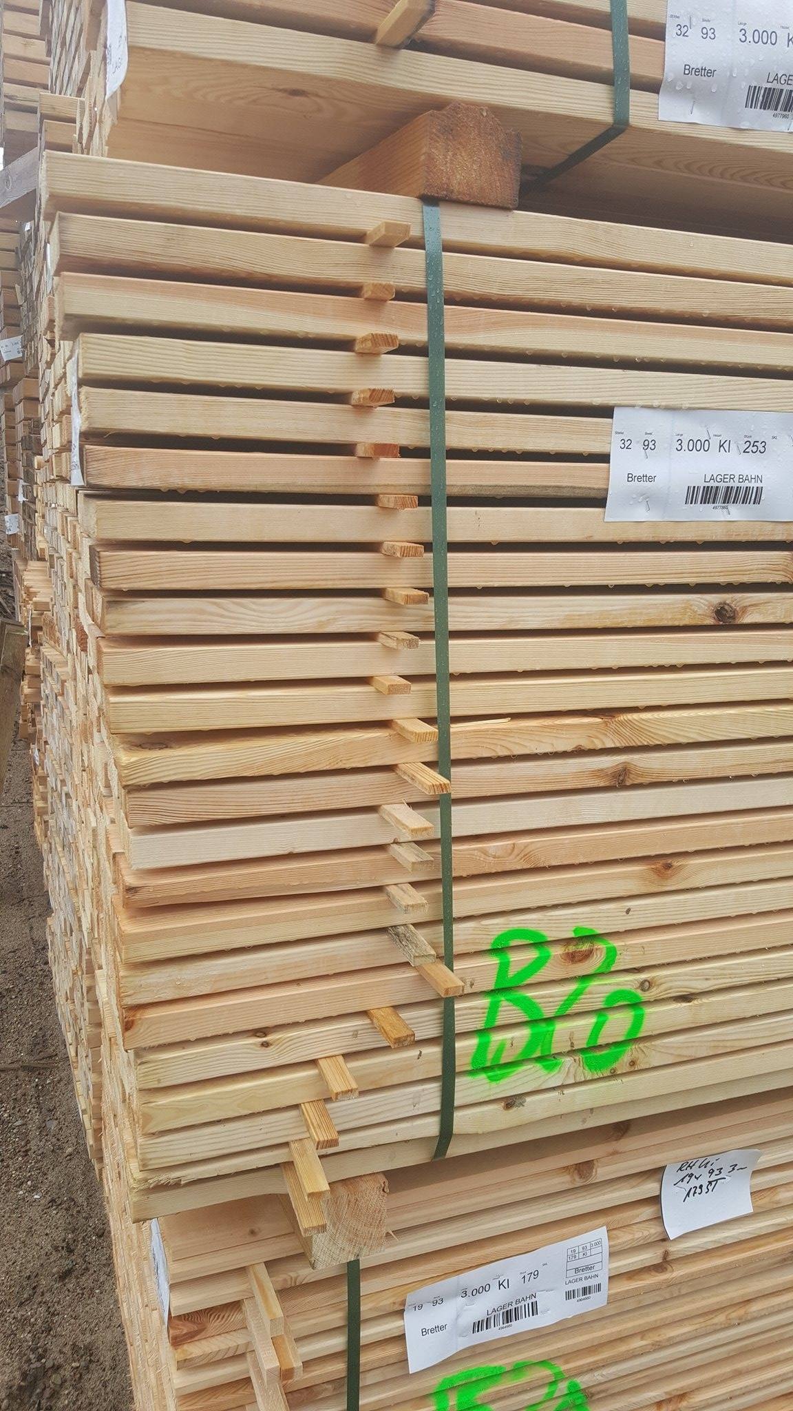 Stos tarcicy budowlanej, zabezpieczony zieloną taśmą, z widocznymi etykietami informacyjnymi i zielonymi oznaczeniami na niektórych deskach.