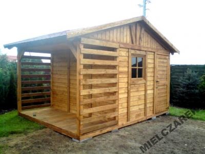 Drewniana altana ogrodowa z zadaszoną werandą, widoczne poziome deski tworzące ażurową ścianę werandy, małe okno i drzwi do pomieszczenia gospodarczego. Na trawniku widoczny cień. Na dolnym brzegu...