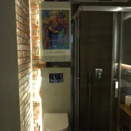 Nowoczesna łazienka z toaletą podwieszaną, kabiną prysznicową z drewnopodobnymi panelami i ceglaną ścianą z plakatem kolarza.