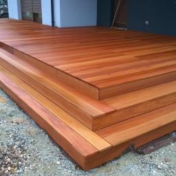 Kostroma - Nowoczesny taras z drewna egzotycznego z trzema schodkami, ułożony na żwirowym podłożu przy budynku z szarą elewacją.