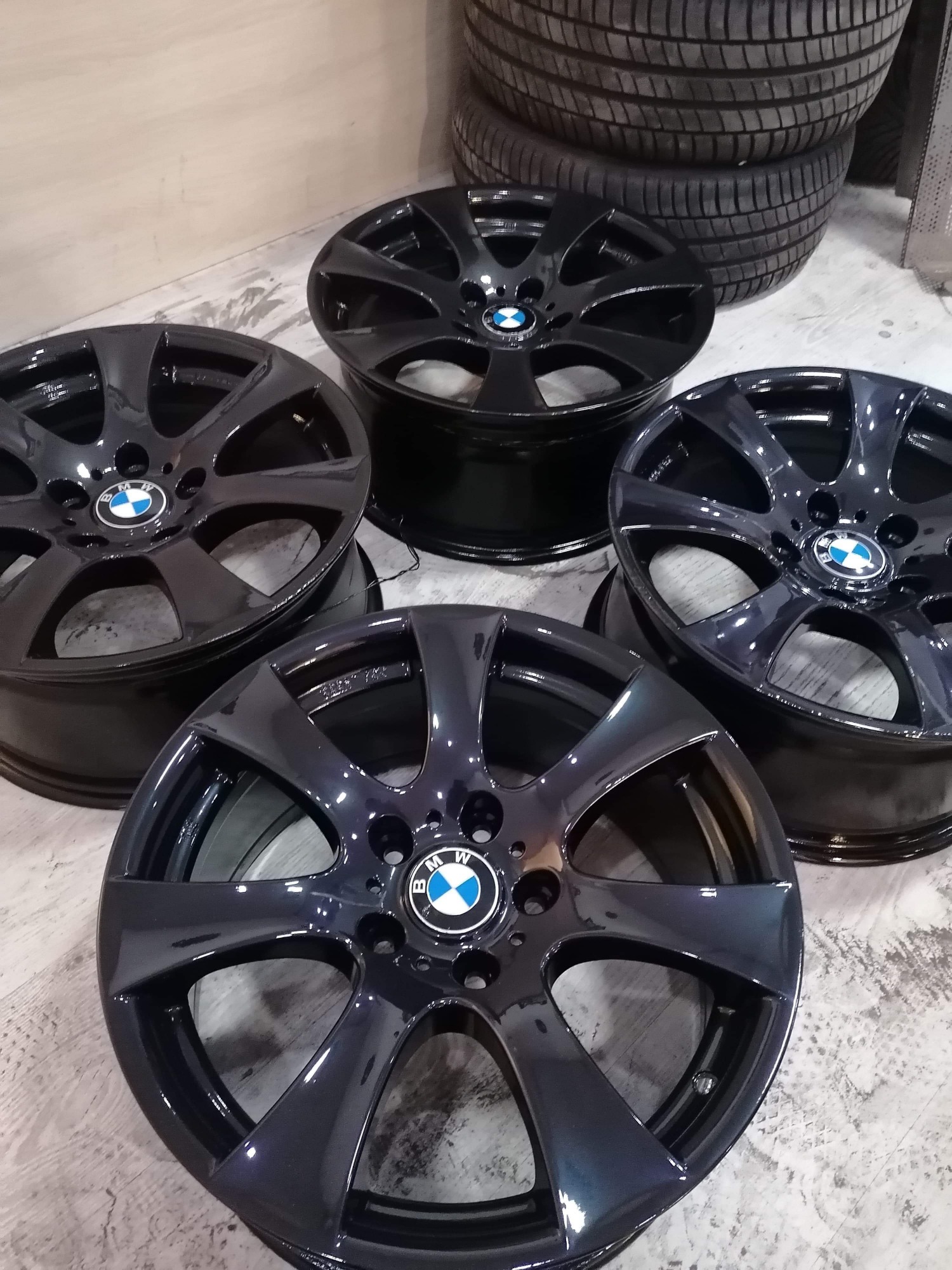 Cztery czarne, błyszczące felgi aluminiowe BMW z oponami w tle, po renowacji i lakierowaniu.