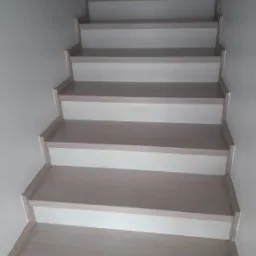 Schody z jasnego drewna z białymi podstopnicami, widok z dołu, minimalistyczny design.