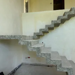 Surowe, betonowe schody wspornikowe w trakcie montażu na tle świeżo otynkowanych ścian wewnętrznych, widoczne przewody elektryczne i niedokończone wykończenie.