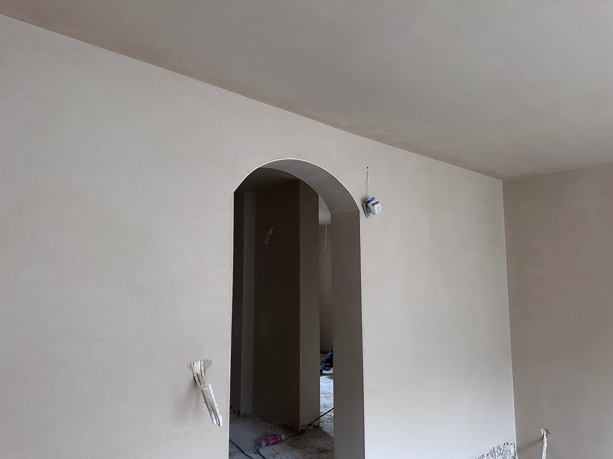 Świeżo położone, jasne tynki maszynowe w łukowatym przejściu w Nowej Soli, z widocznymi przewodami elektrycznymi i fragmentem podłogi w trakcie prac wykończeniowych.