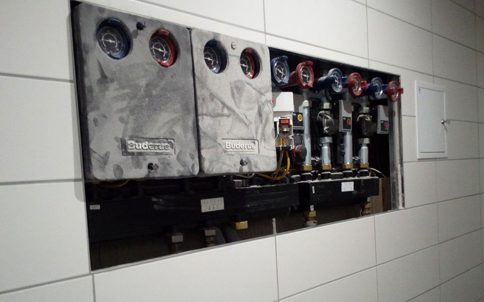 Wnęka w wykafelkowanej ścianie, w której zamontowano rozdzielacz ogrzewania podłogowego marki Buderus z manometrami i zaworami regulacyjnymi.
