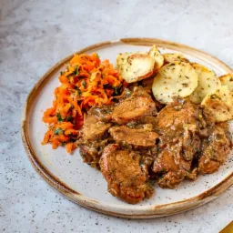 Danie obiadowe z mięsem w sosie, pieczonymi ziemniakami z ziołami i surówką z marchewki, serwowane na talerzu w Siedlcach.