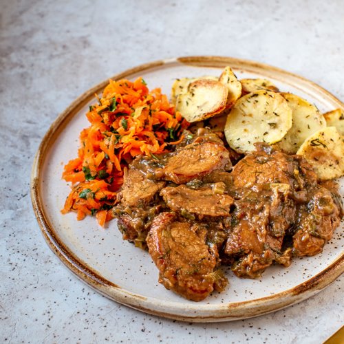 Danie obiadowe z mięsem w sosie, pieczonymi ziemniakami z ziołami i surówką z marchewki, serwowane na talerzu w Siedlcach.