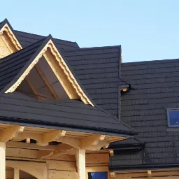 Fragment dachu z czarną dachówką modułową na drewnianym domu w stylu góralskim, widoczne detale wykończenia lukarn i rynny.