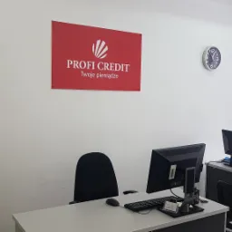 Biuro firmy pożyczkowej z logo Profi Credit na ścianie, dwa stanowiska pracy z komputerami i zegar na ścianie.