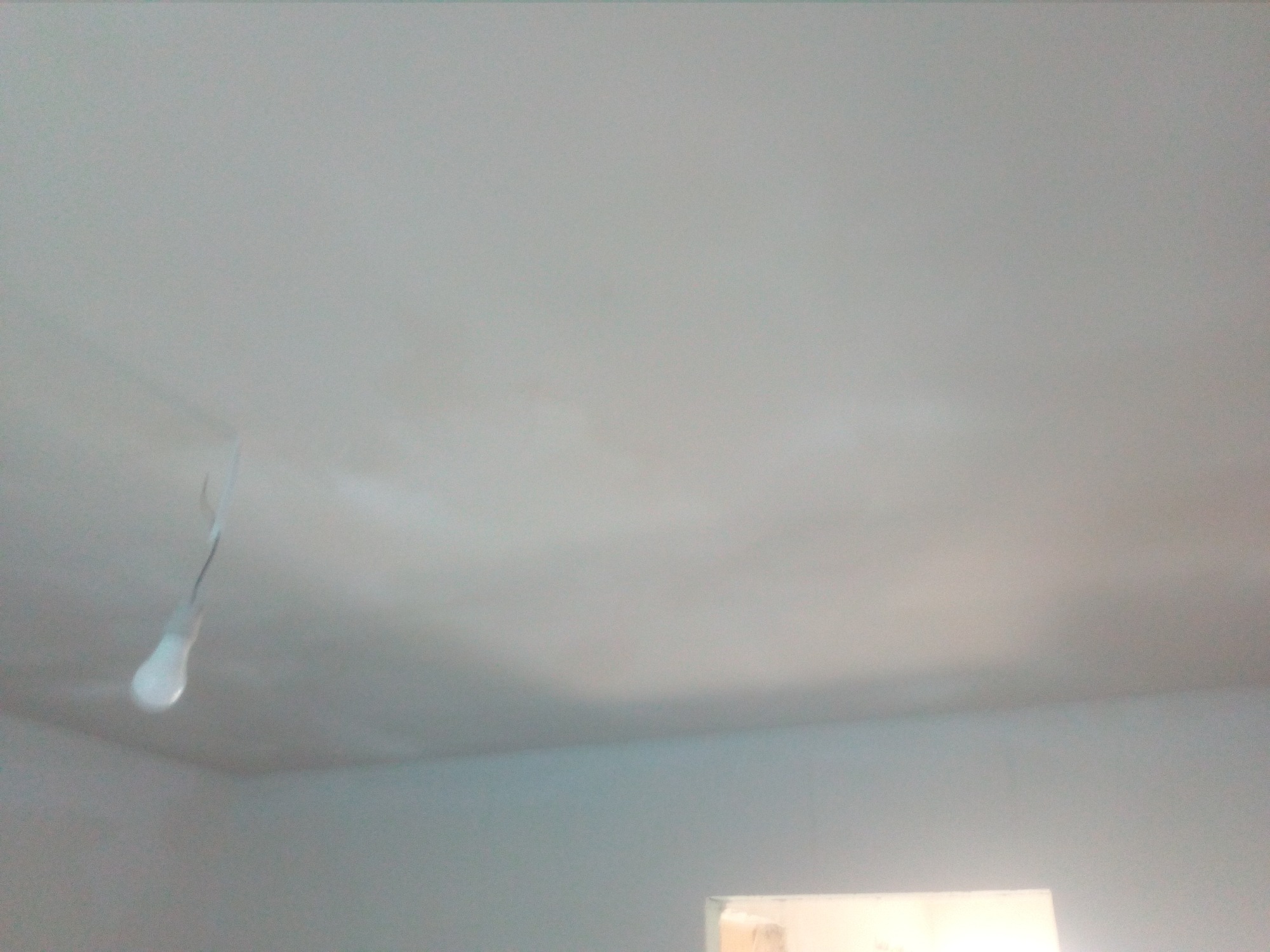 Świeżo wyszpachlowany sufit z widocznymi smugami, w rogu wisząca żarówka na kablu.