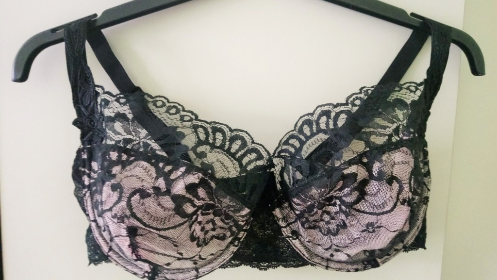 Czarny koronkowy biustonosz z różową podszewką, wiszący na czarnym wieszaku.