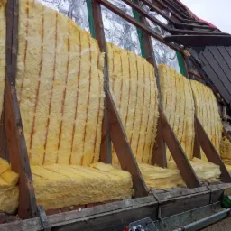 Poddasze z widoczną izolacją z wełny mineralnej pomiędzy krokwiami, częściowo odkryty dach z dachówki bitumicznej i blachy trapezowej.