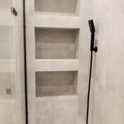 Wykończona łazienka z szarymi płytkami, wnękami w ścianie i czarną armaturą prysznicową.