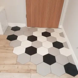 Ułożona podłoga z heksagonalnych płytek w odcieniach szarości, bieli i czerni, przechodząca w drewnopodobne panele, widok na fragment drzwi.