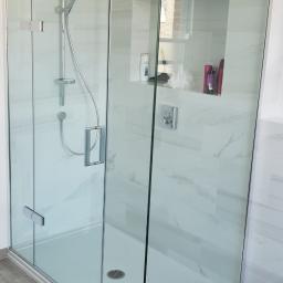 Dariusz Wysocki - Nowoczesna kabina prysznicowa z przezroczystego szkła, chromowane wykończenia, białe płytki imitujące marmur oraz wnęka na kosmetyki w ścianie.