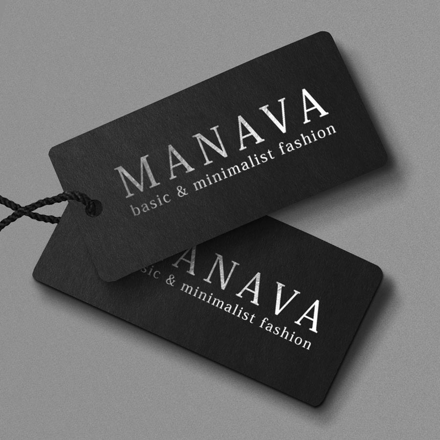 Dwie czarne metki odzieżowe z srebrnym napisem 'MANAVA basic & minimalist fashion', połączone czarnym sznurkiem, leżące na szarym tle.