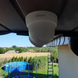 Kamera kopułkowa Dahua zamontowana pod okapem domu, widok na ogród z basenem i trampoliną.