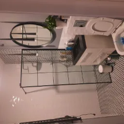 Nowoczesna łazienka z kabiną prysznicową typu walk-in z czarnymi profilami, umywalką z szafką, toaletą, okrągłym lustrem z podłużnymi lampami i geometryczną tapetą w odcieniach bieli i czerni.