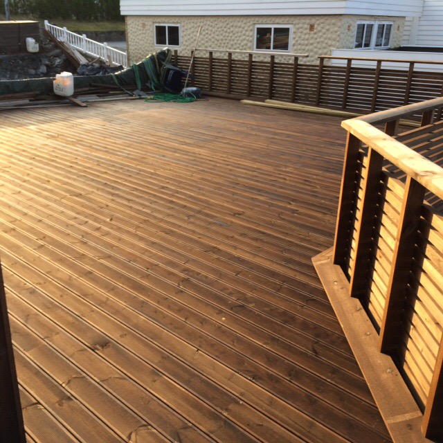 Nowo wybudowany taras drewniany z barierkami, widok z góry, w tle dom jednorodzinny i materiały budowlane.