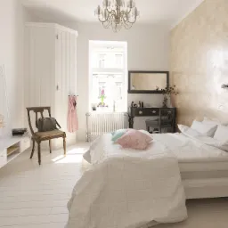 Jasne wnętrze sypialni z łóżkiem, toaletką i dekoracyjną ścianą z efektem rosy, oświetlone światłem dziennym wpadającym przez okno.