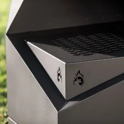 Nowoczesny, geometryczny grill ogrodowy z logo byka w płomieniach, ustawiony na trawie.