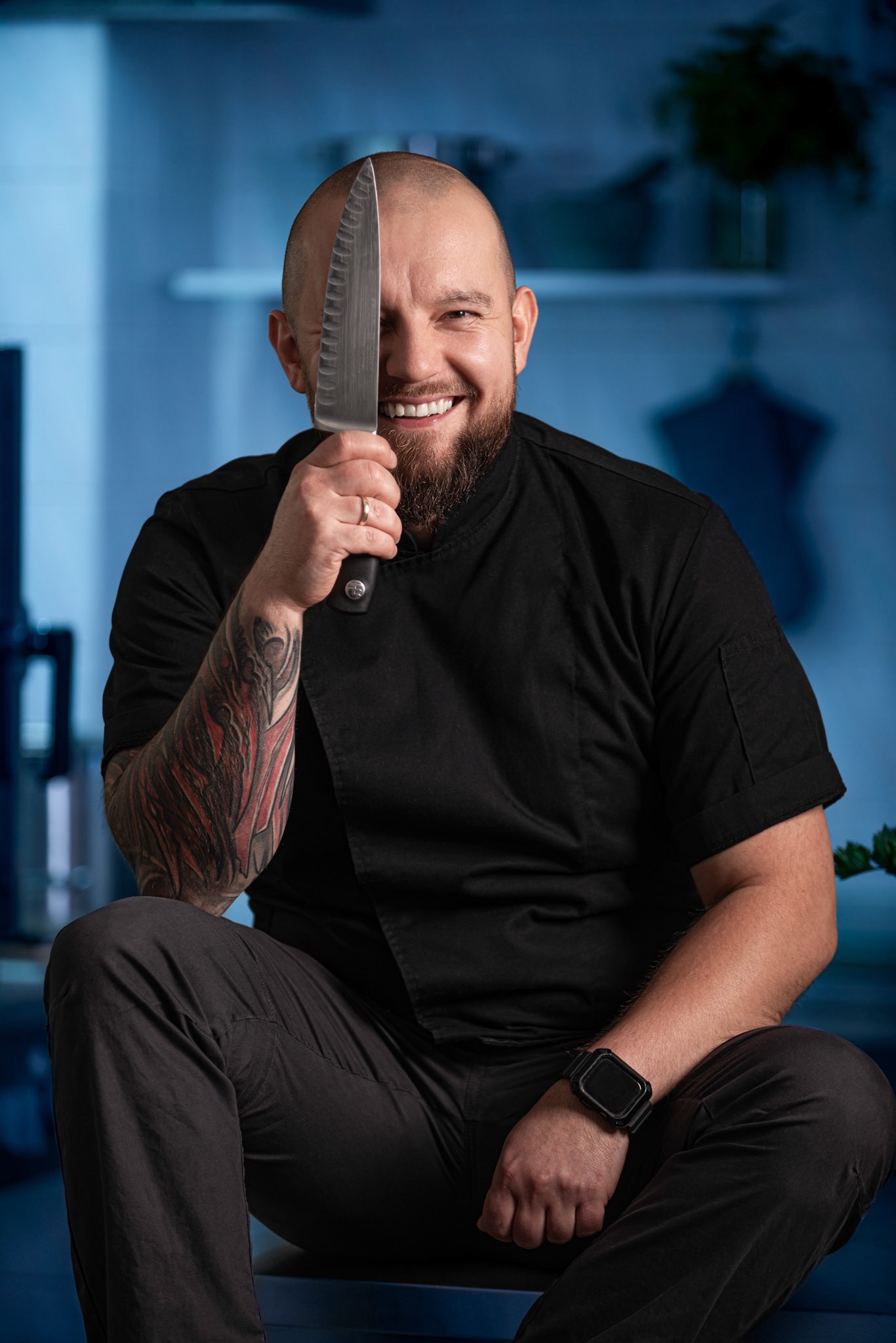 Portret uśmiechniętego kucharza z tatuażem na ramieniu, trzymającego nóż przed twarzą w Zielonej Górze.