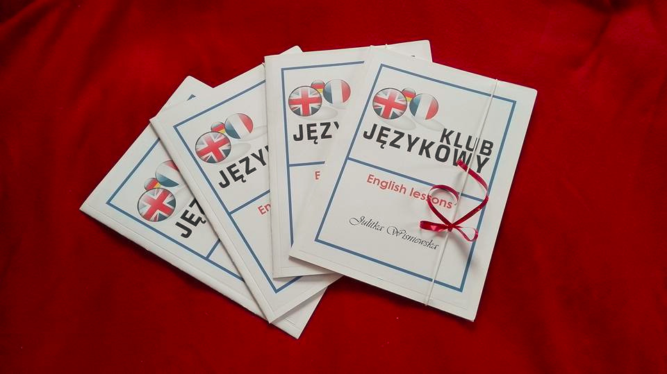Stos czterech broszur z napisem 'Klub Językowy' i ilustracjami flag Wielkiej Brytanii, Francji i Niemiec, przewiązanych czerwoną wstążką, na czerwonym tle.