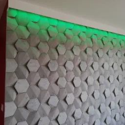 Dekoracyjna ściana z betonowych heksagonów oświetlona od góry zielonym światłem LED, widok na część ściany i narożnik pokoju.