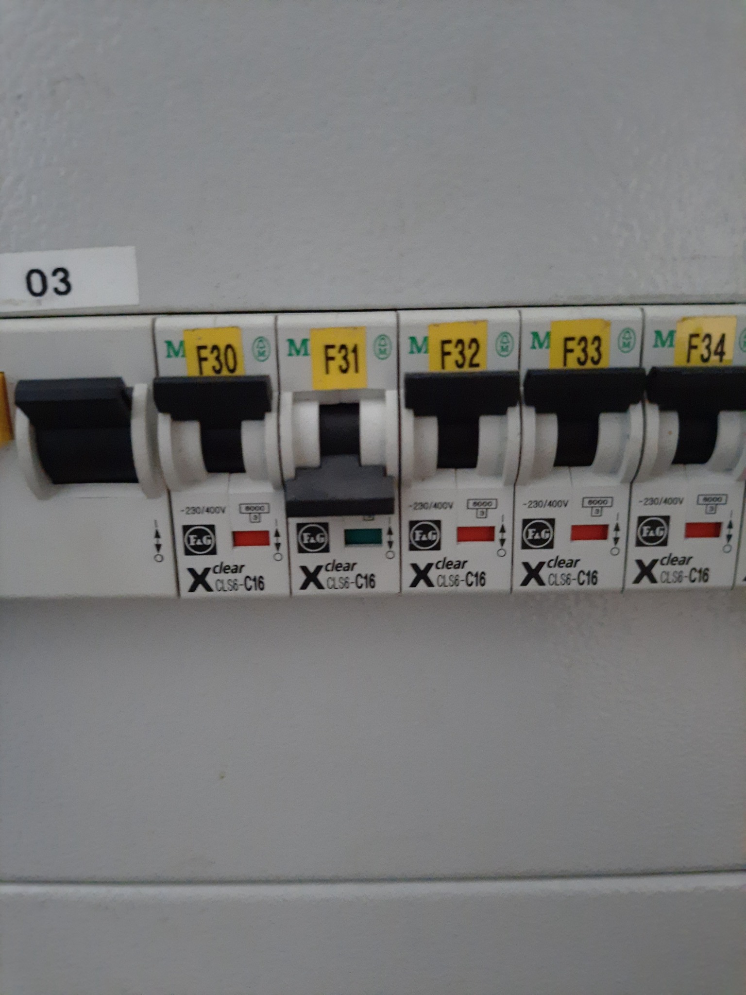 Szczegółowe ujęcie tablicy elektrycznej z wyłącznikami oznaczonymi F30 do F34, jeden wyłącznik w pozycji wyłączonej, pozostałe włączone, widoczne oznaczenia napięcia i prądu.