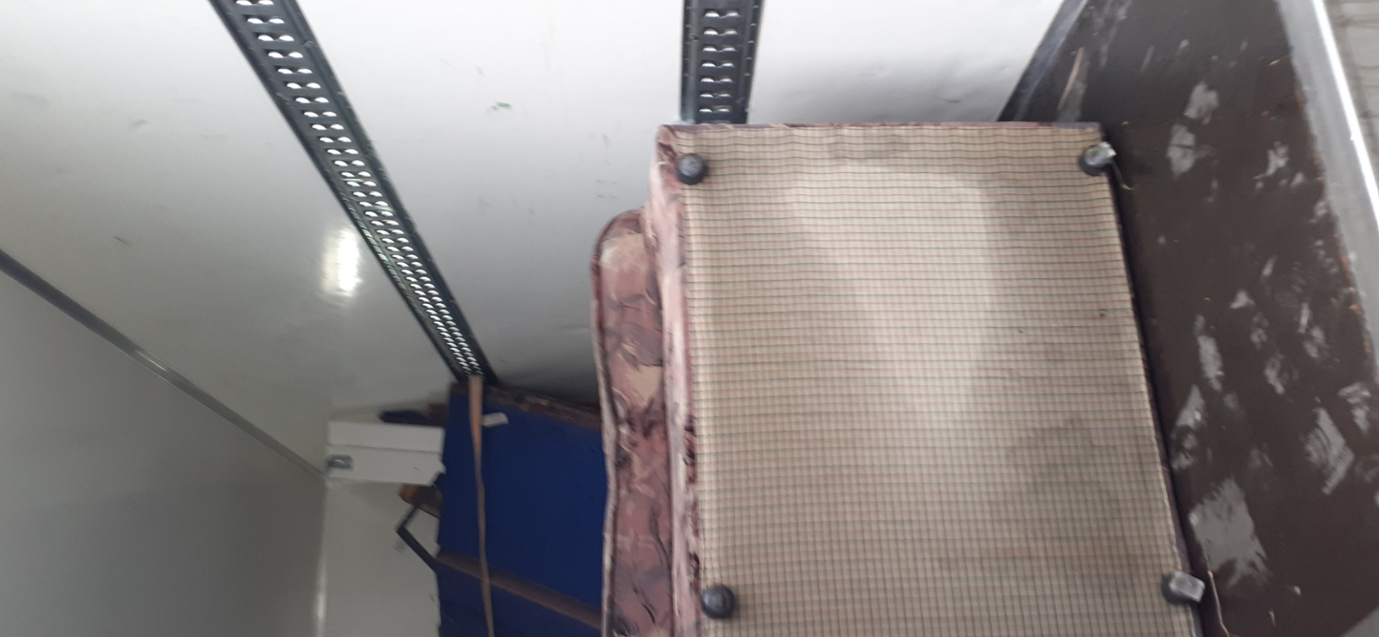 Wnętrze przestrzeni ładunkowej pojazdu z częściowo załadowanym tapicerowanym meblem, widoczne mocowania na ścianach.