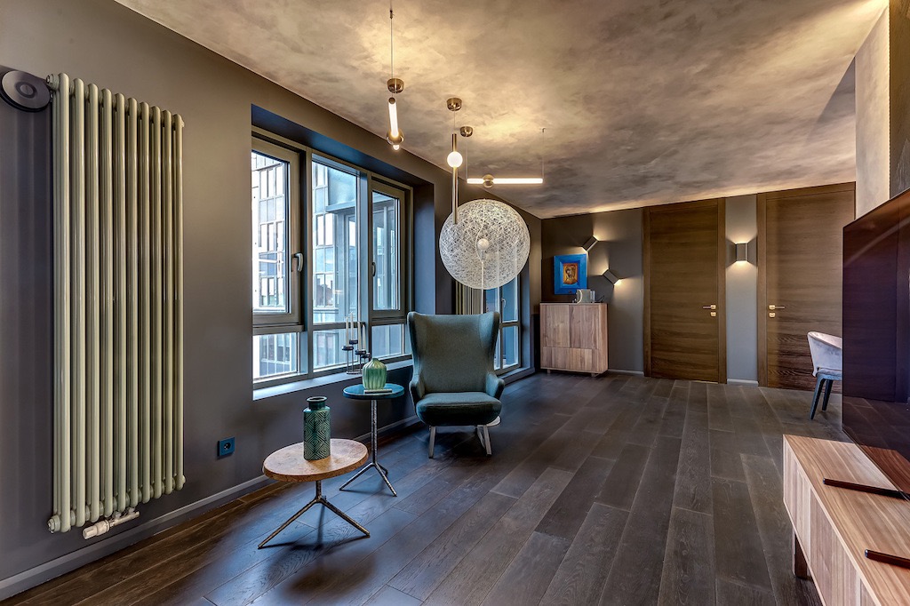 Stylowe wykończenie wnętrza w Warszawie: ciemna podłoga, szare ściany, designerski grzejnik i oświetlenie. Widok na okno z wysokiego piętra.